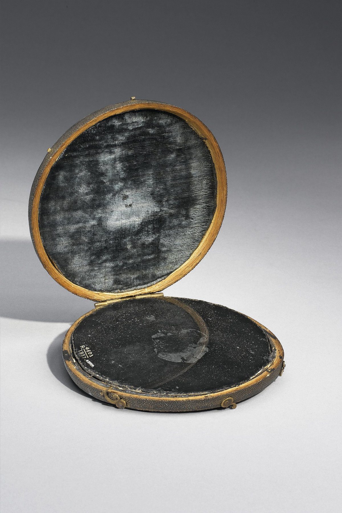 A small round dark mirror in an open gilt-edged sharkskin case
