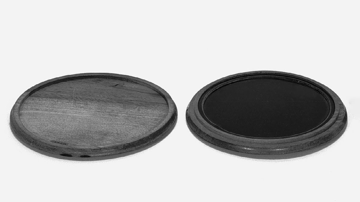 A round black Claude glass beside its turned wooden case