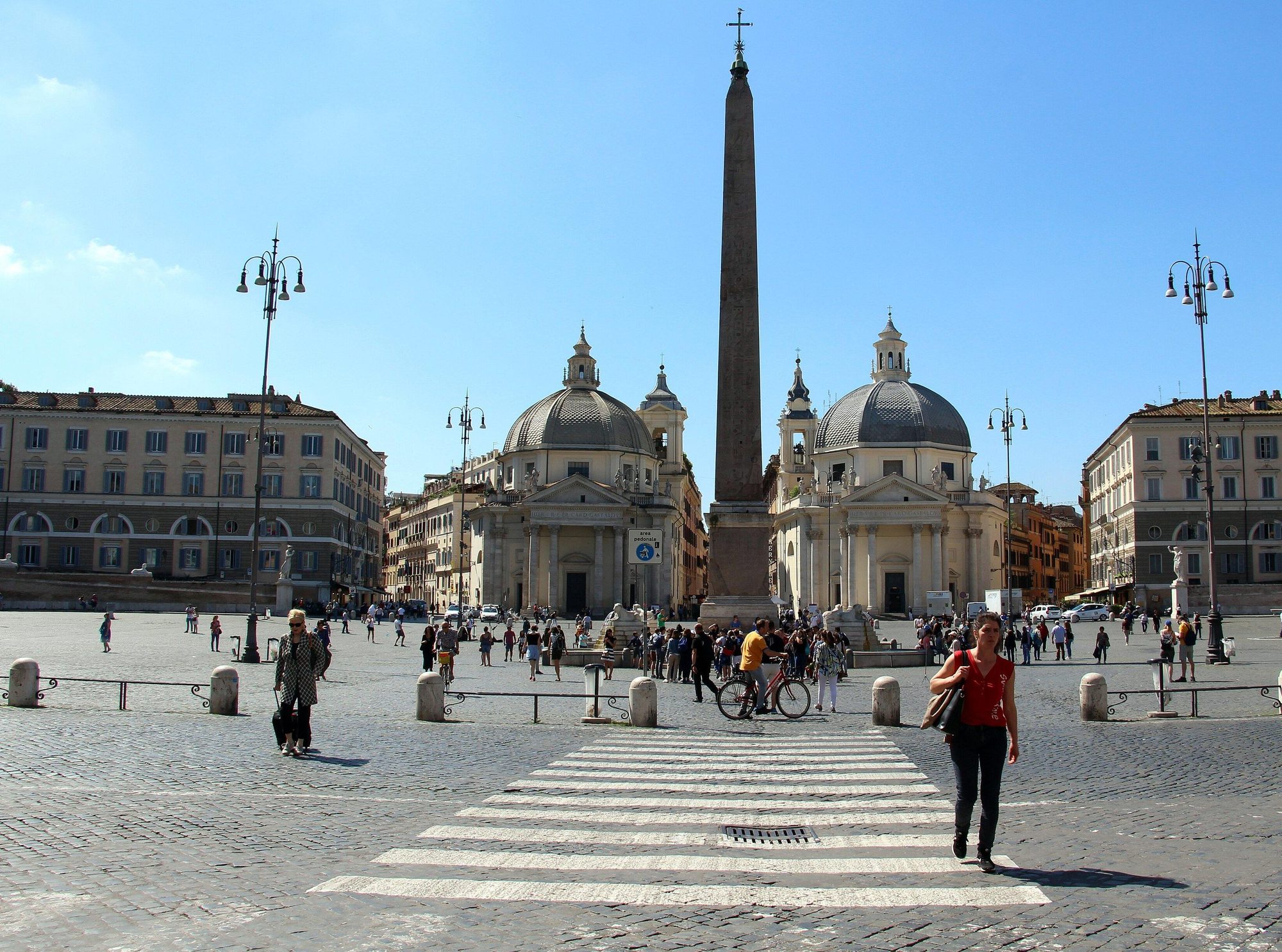 The Piazza del Popolo today, a wide paved square with the obelisk and the two domed churches under a blue sky